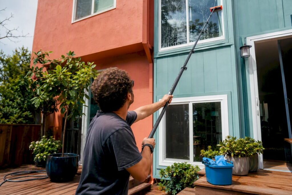 Person cleaning exterior window with extension pole